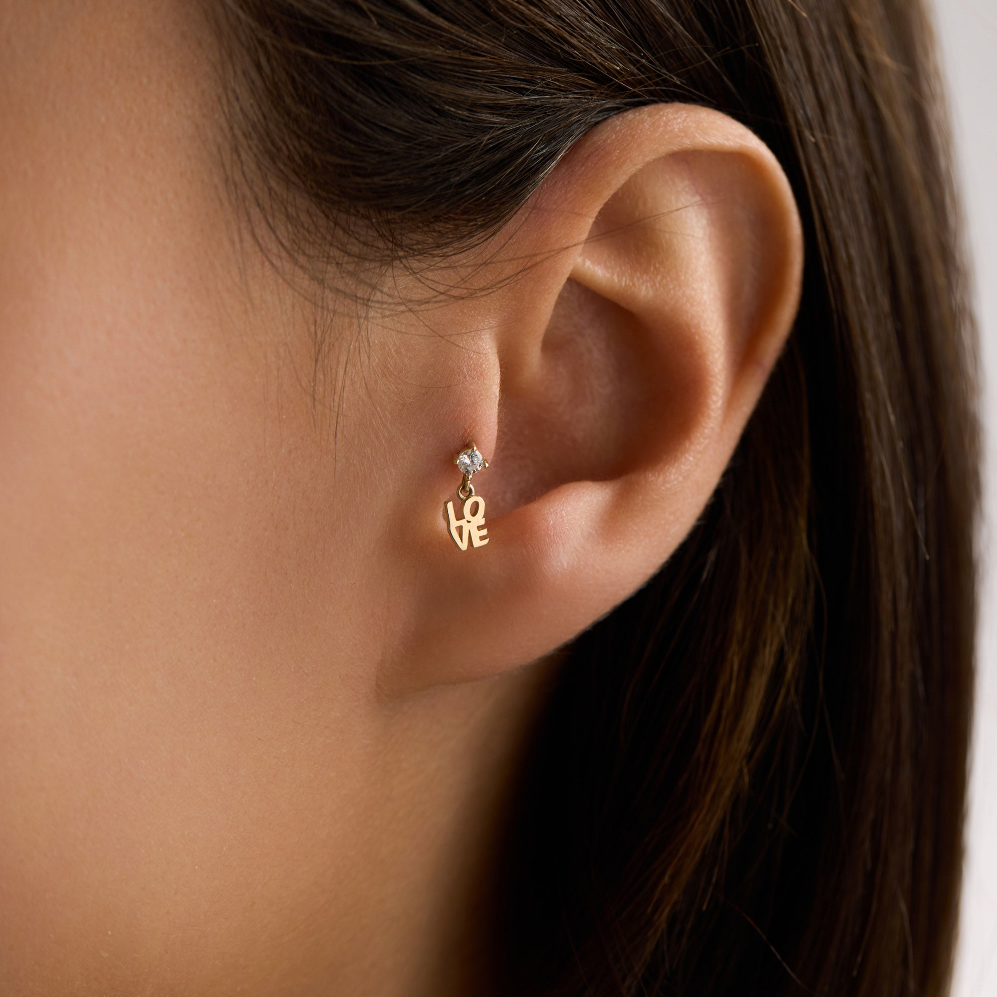 Gold 'LOVE' Piercing worn by a woman on tragus ear with dark hair.