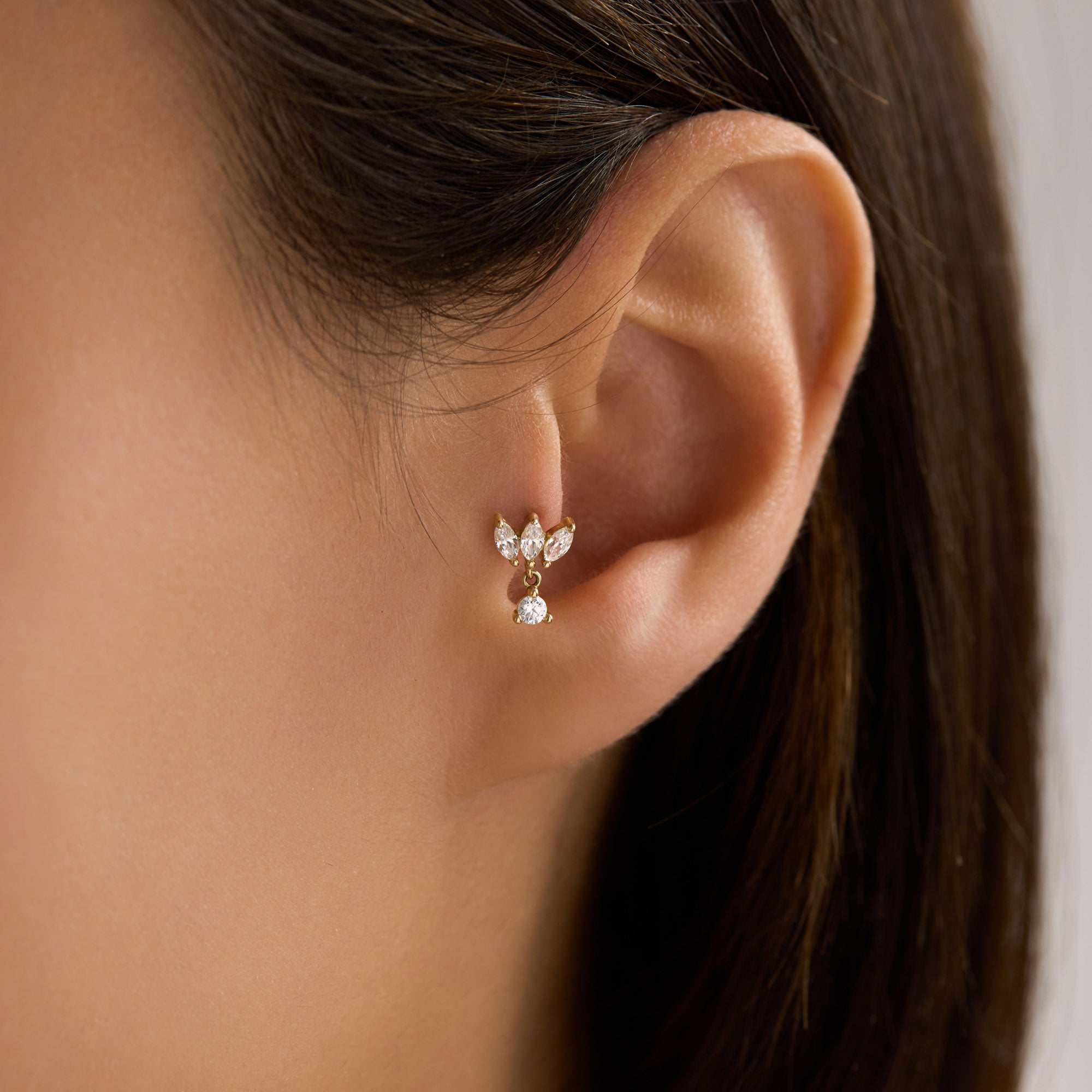 Close-up of an ear wearing a gold Marquise Piercing on tragus with a visible Avora Fine Jewelry logo.
