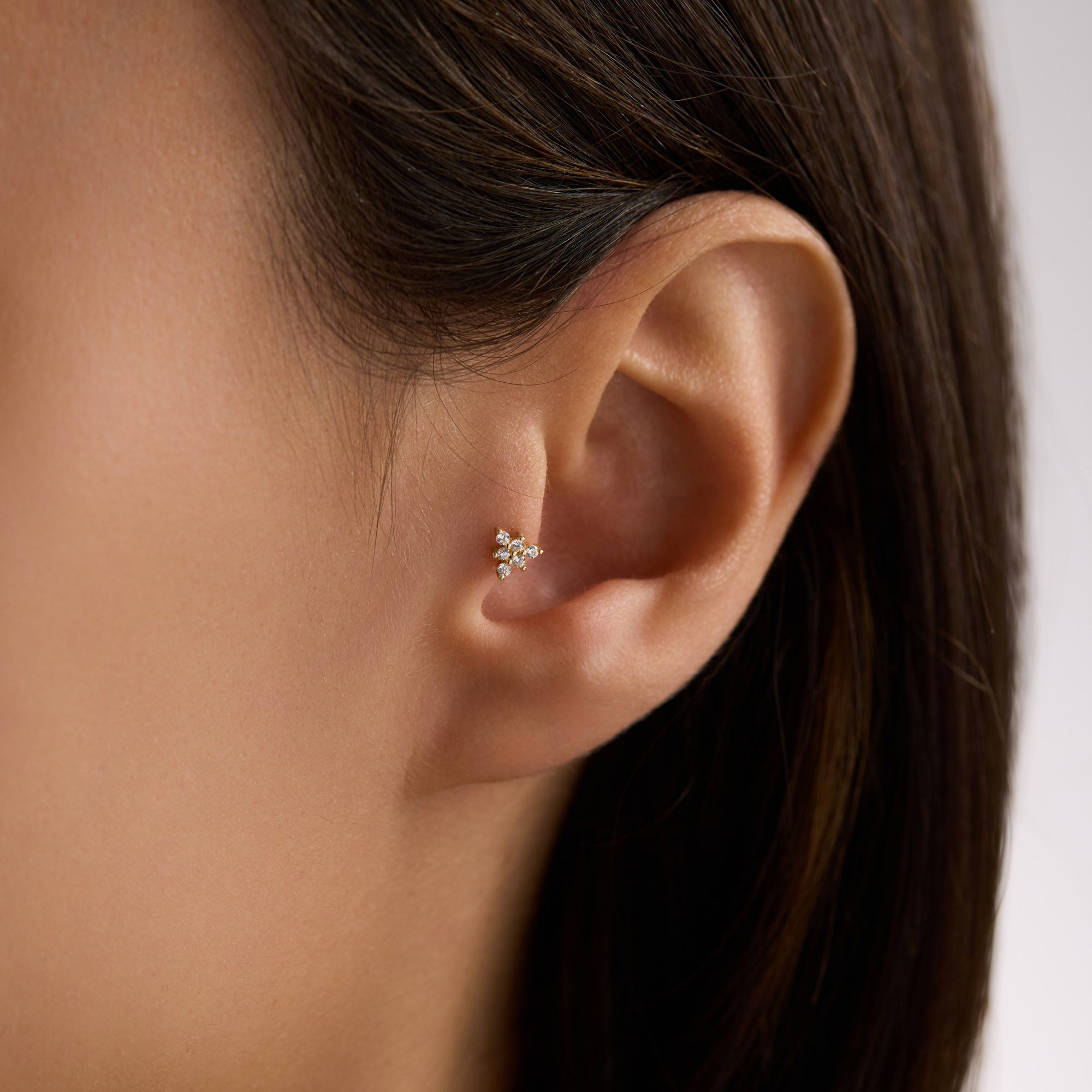 Close-up of an ear wearing a 14K Solid Gold Floral Triangle CZ Cluster Piercing with 'Avora Fine Jewelry' branding.