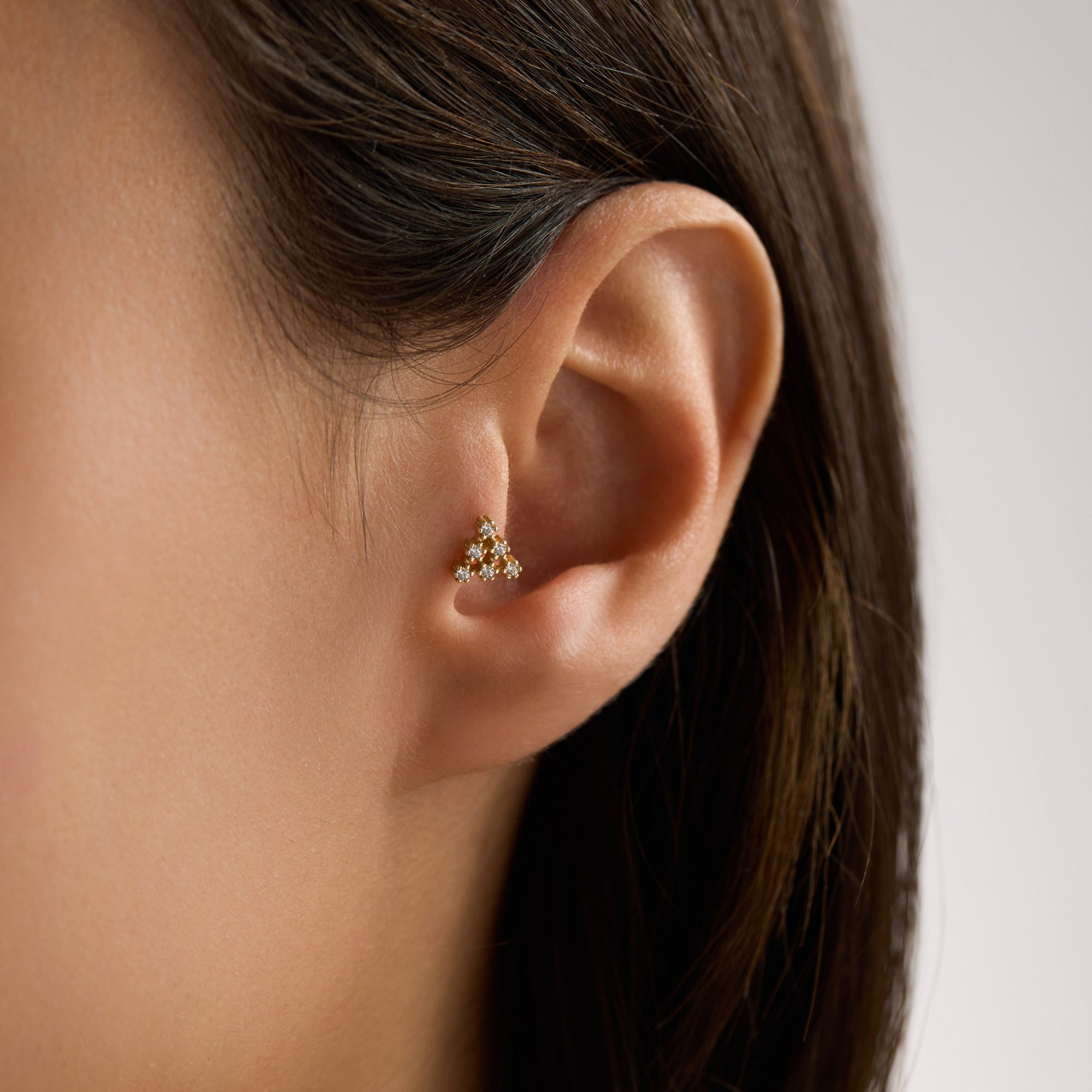 Close-up of an ear tragus wearing a small 14K solid gold triangle CZ cluster tragus piercing with 'Avora Fine Jewelry' branding.