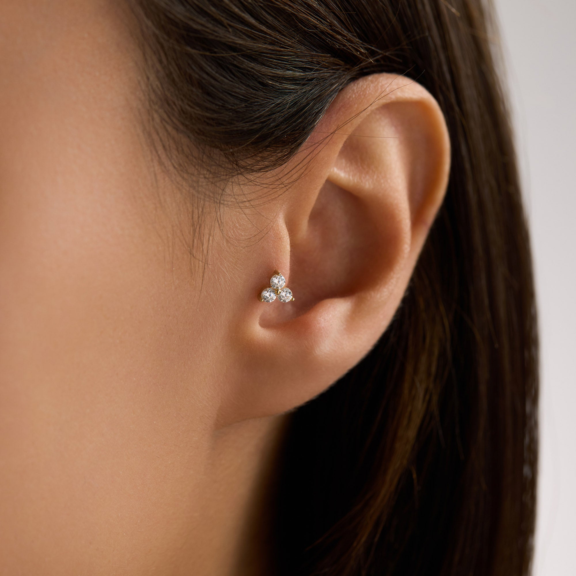 Close-up of an ear wearing a 14K solid gold trinity CZ cluster piercings on the tragus