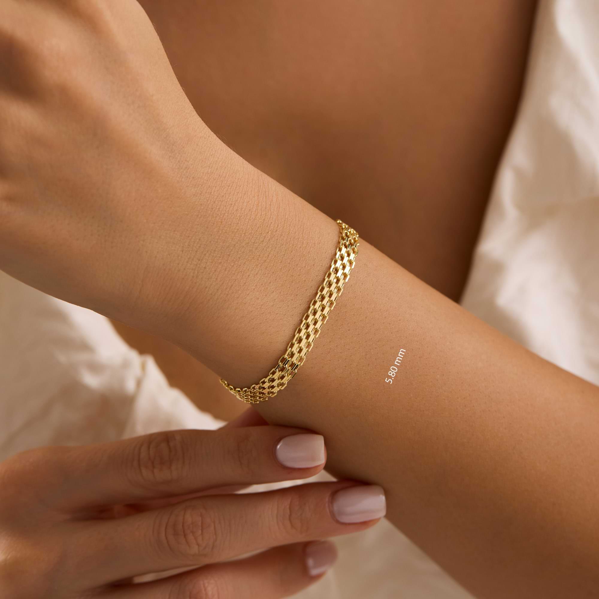Gold bismarck 5.8mm chain bracelet on a wrist with a minimalistic gold ring, against a neutral background.