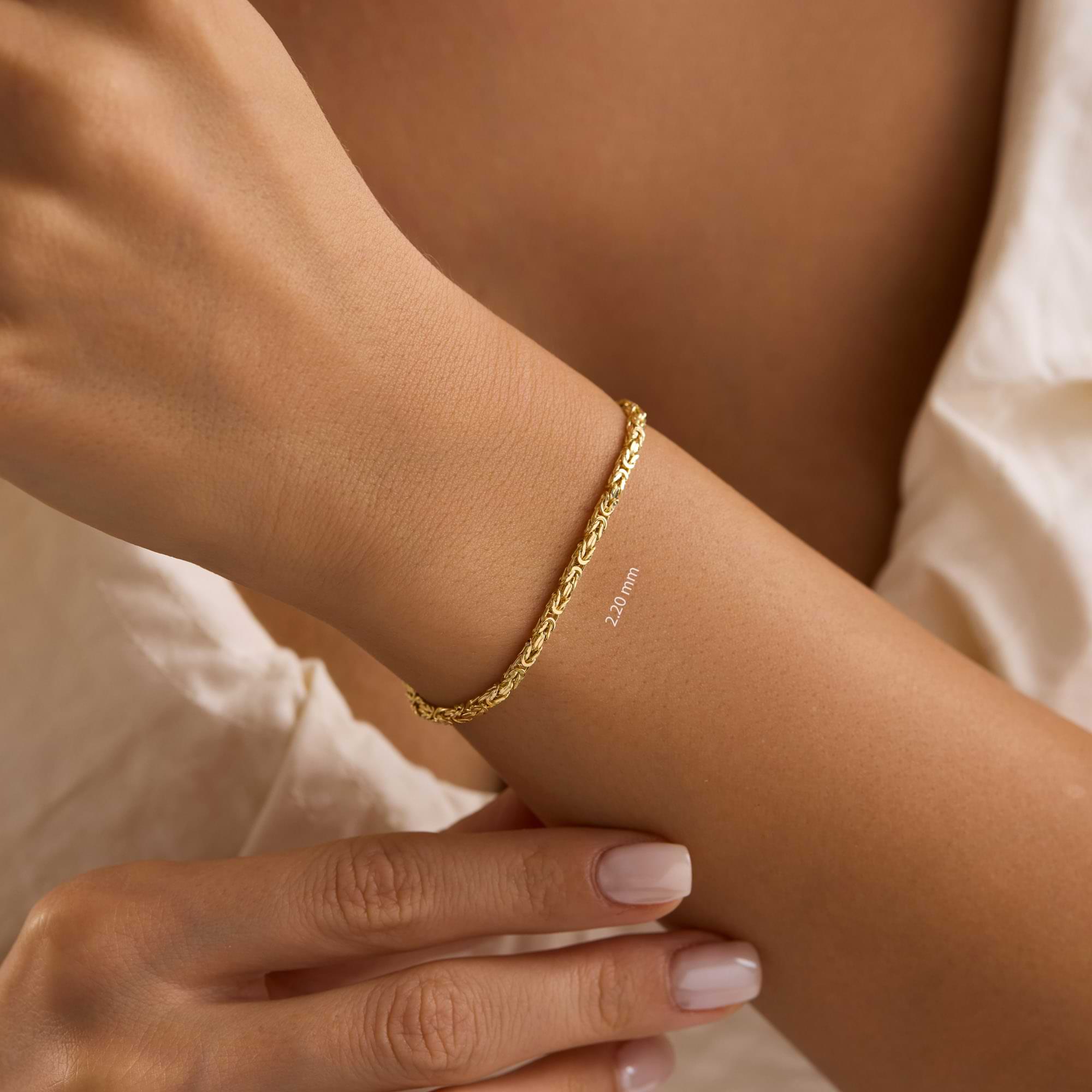 Gold 2.2mm byzantine chain bracelet on a wrist of woman wearing white dress