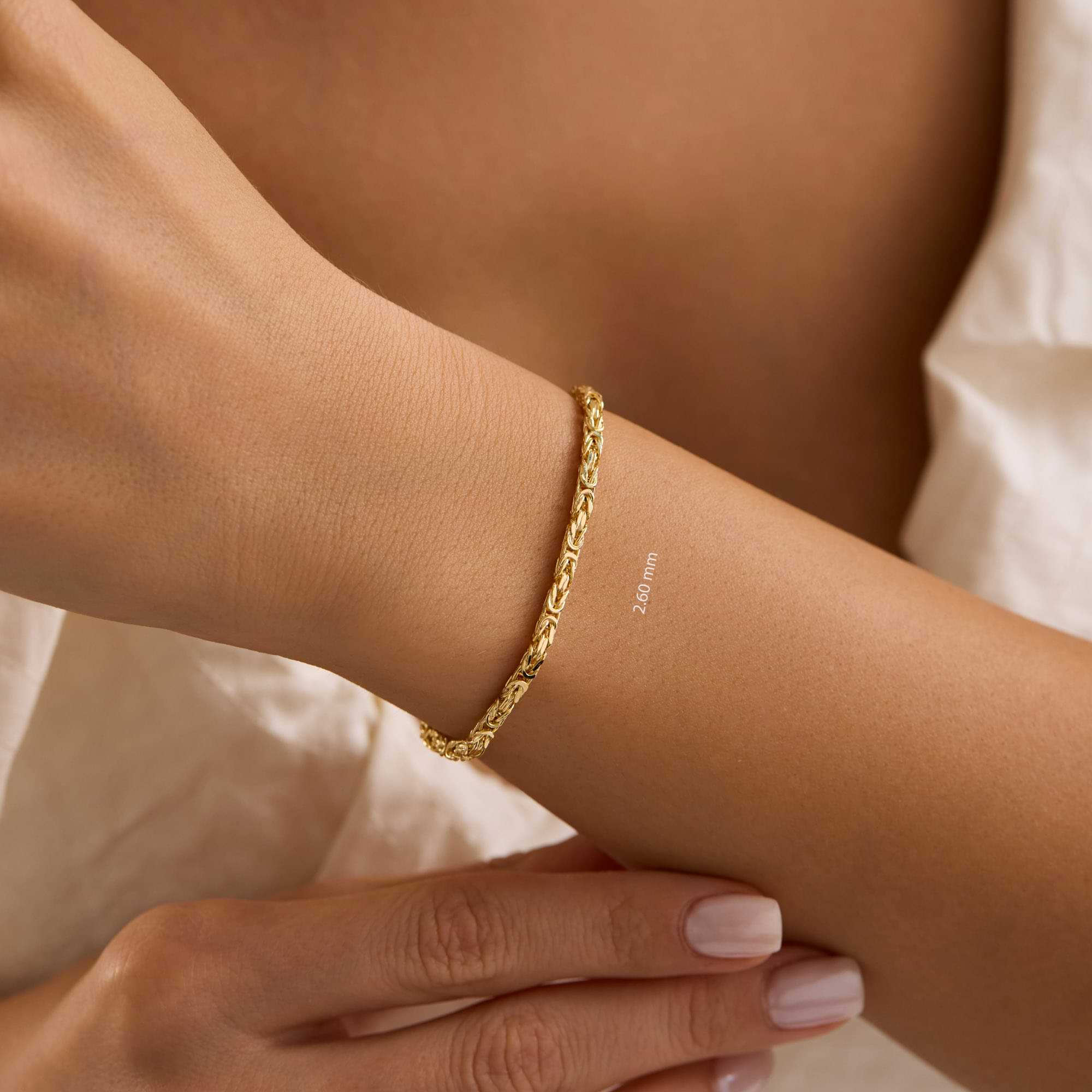 Gold byzantine chain 2.6mm bracelet on a wrist of woman wearing white dress