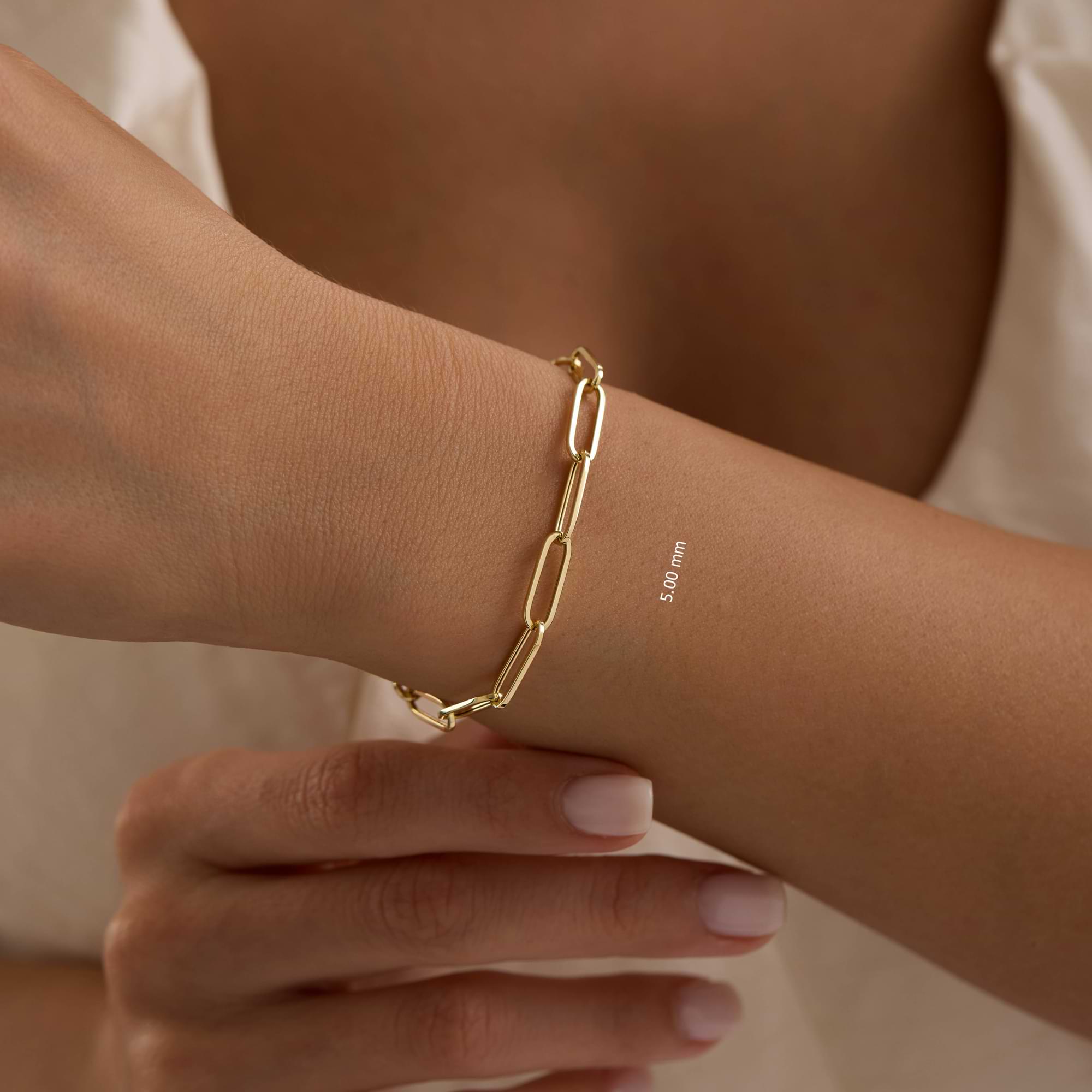 Gold 5mm paperclip chain bracelet on a wrist with a neutral background