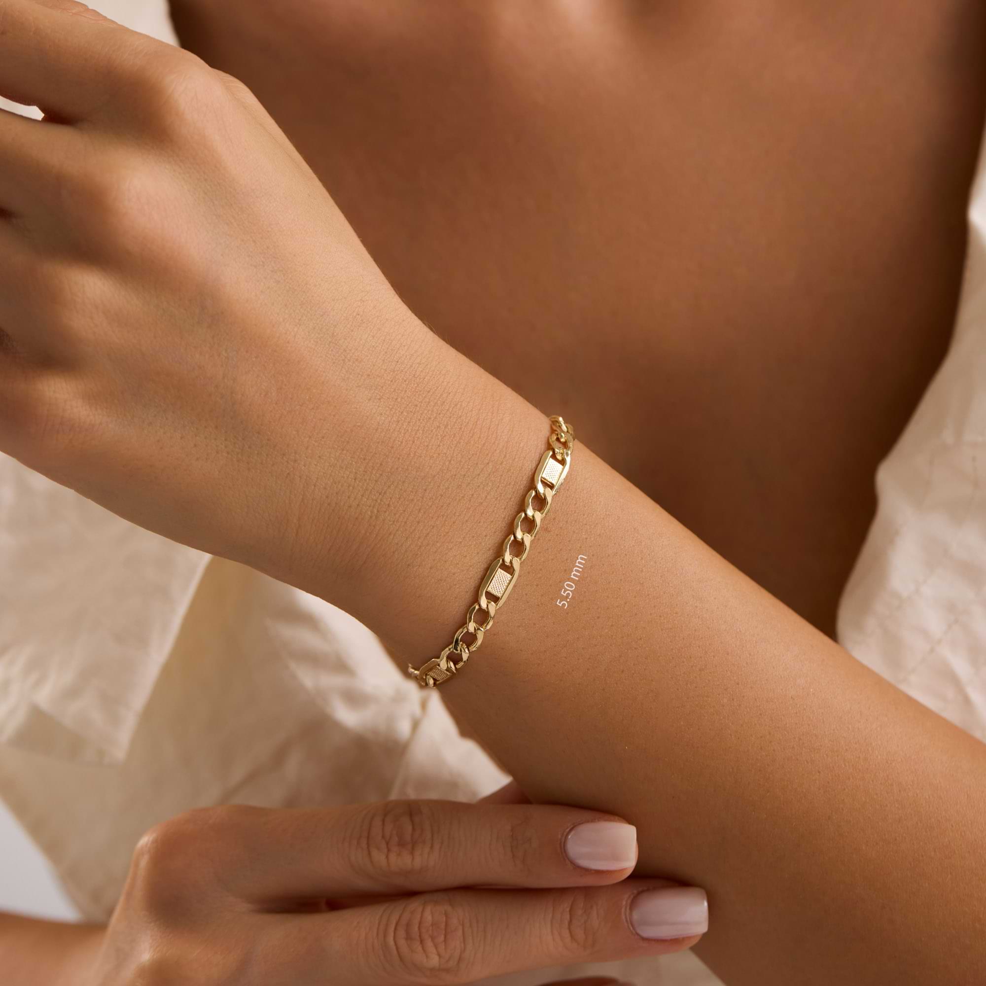 Gold textured figaro 5.5mm bracelet on a wrist of woman wearing white dress.