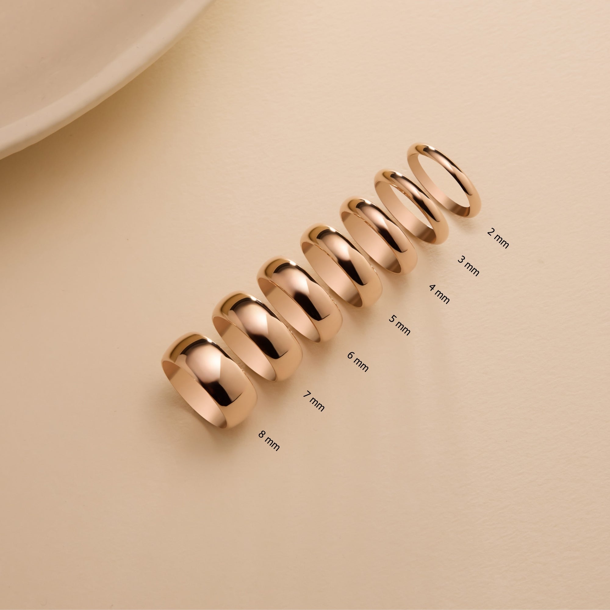 Row of 14k solid rose gold dome wedding bands in sizes 2mm to 8mm displayed on neutral background.