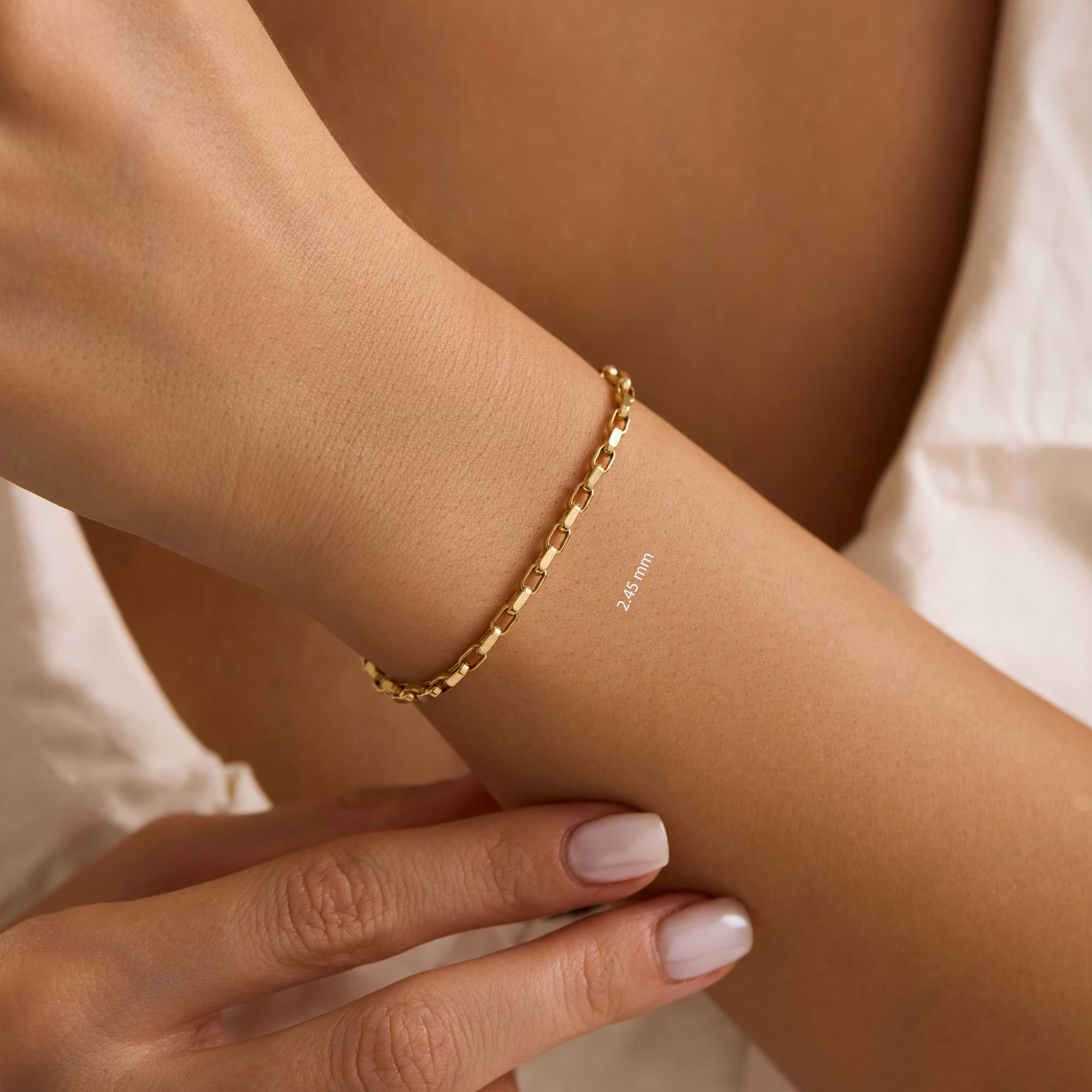 Gold 2.45mm cable bracelet on a wrist with a blurred background