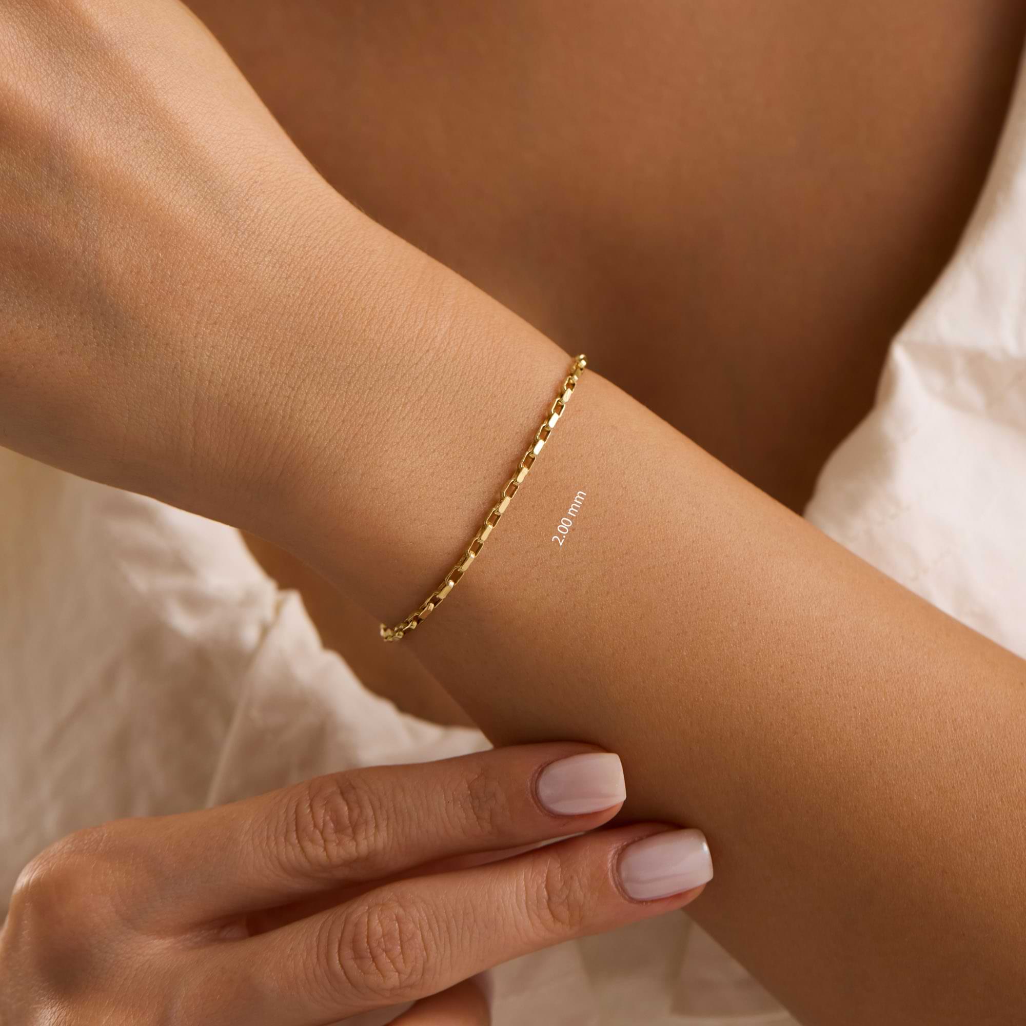 Gold 2mm cable chain bracelet on a wrist of woman wearing white dress