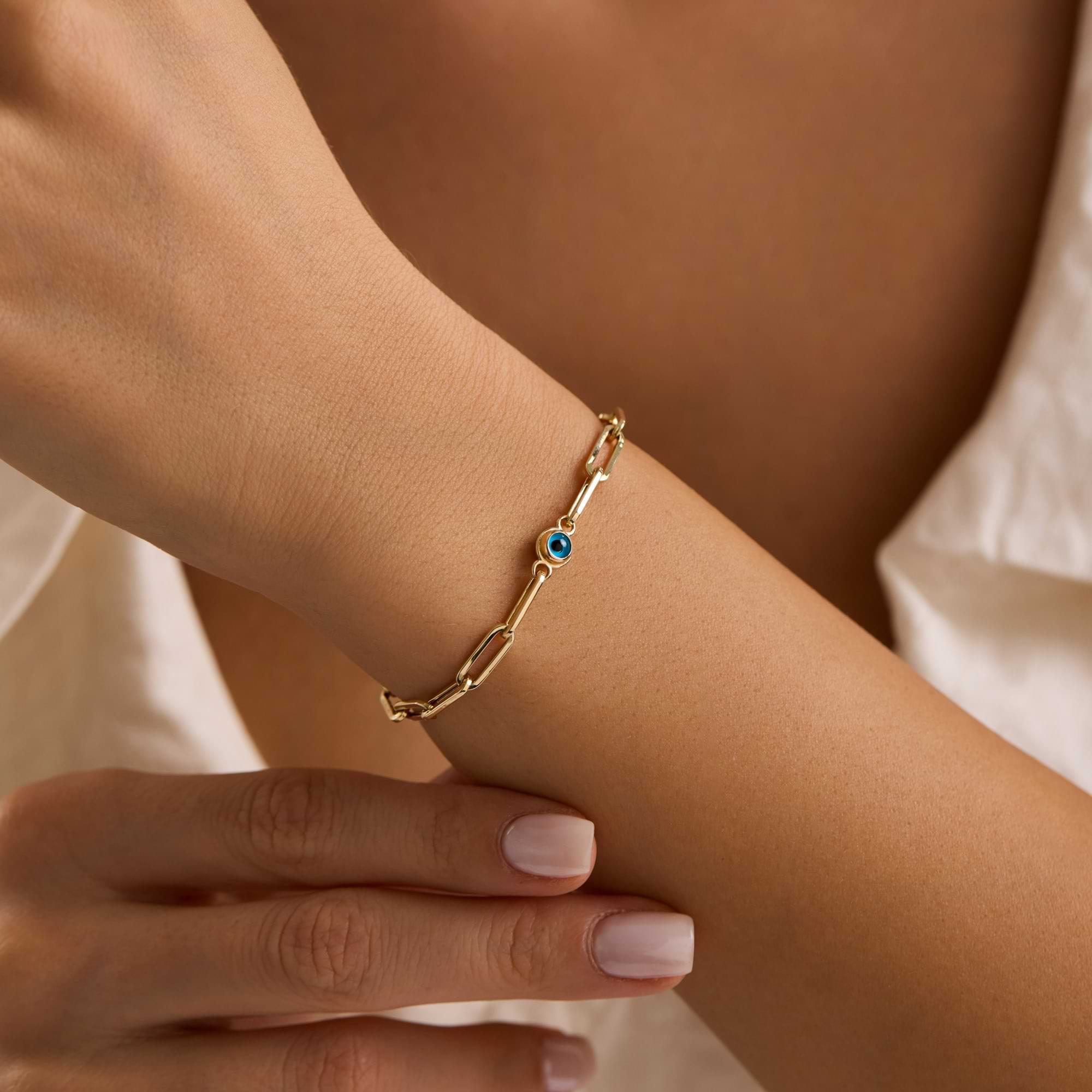 Gold paperclip bracelet with evil eye charms on a woman's wrist 