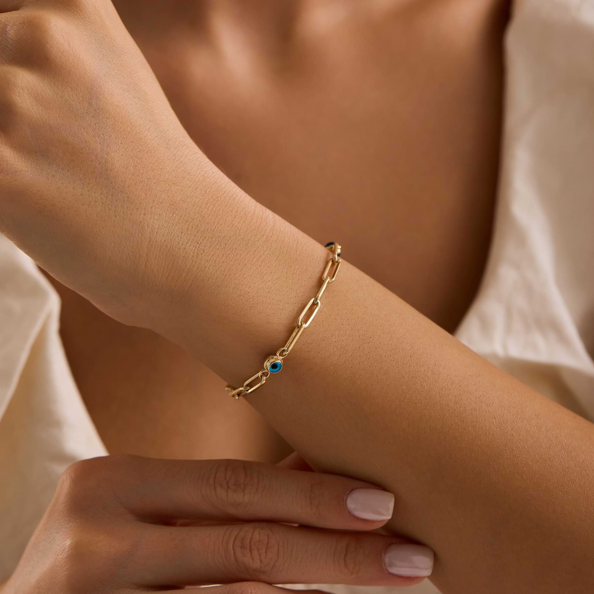 Gold paperclip bracelet with blue eye charms on a woman's wrist 