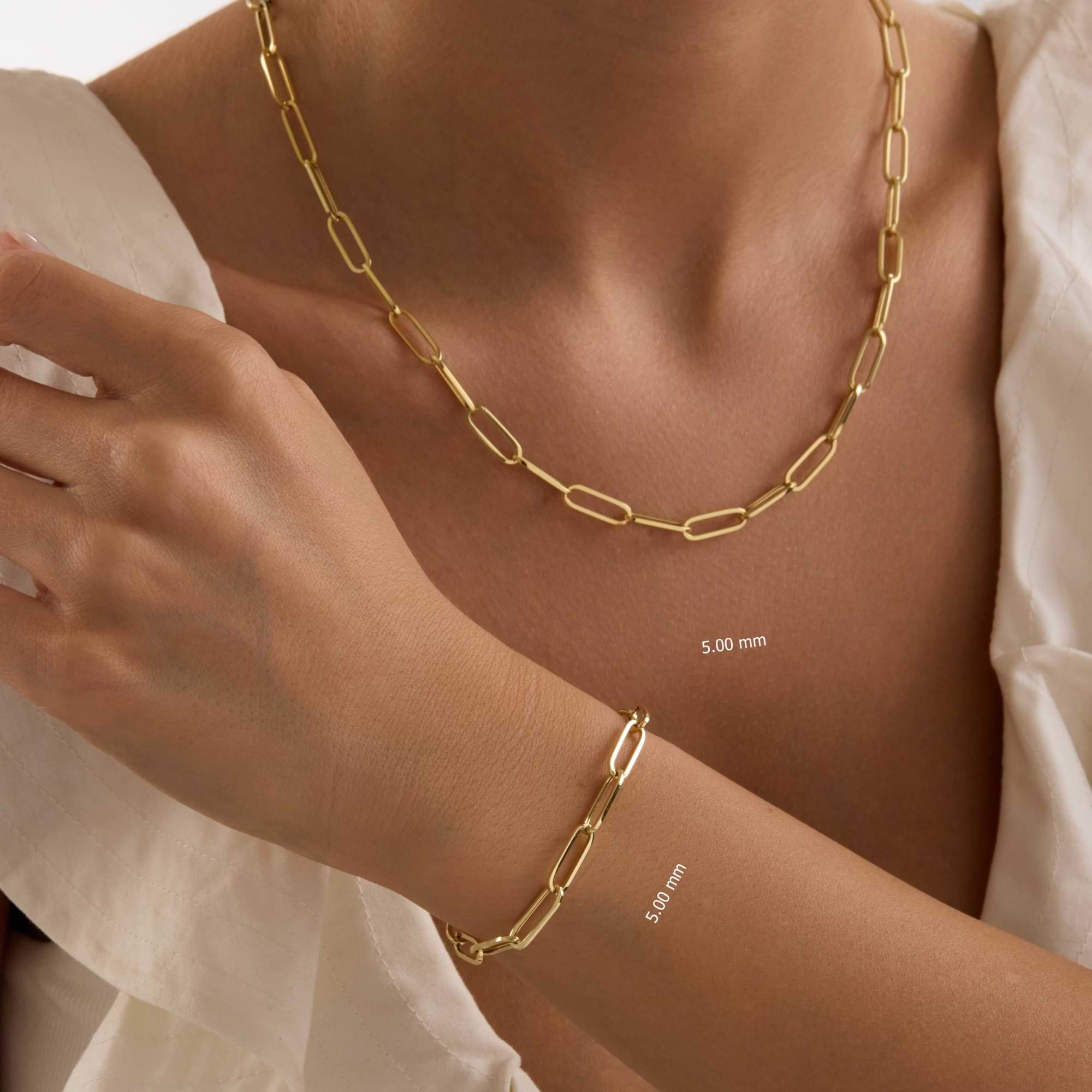 Gold 5mm paperclip chain necklace and bracelet on a person's neck and wrist against a neutral background