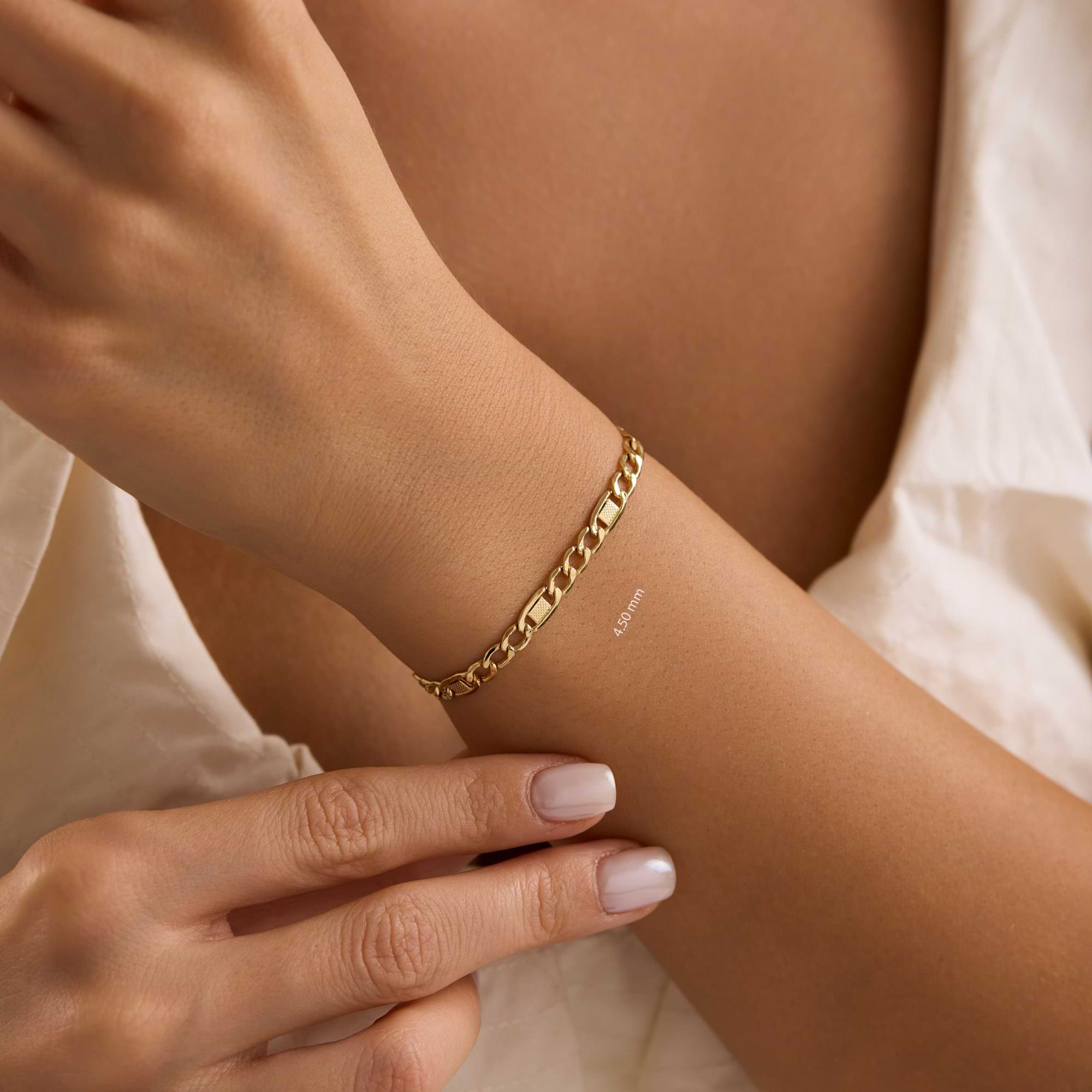 Gold textured figaro 4.5mm bracelet on a wrist of woman wearing white dress.
